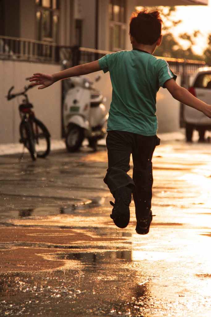 boy in green t shirt running on wet road during daytime